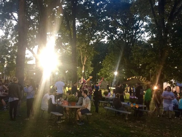 sunlight steams through trees to illuminate students sitting at tables at Homecoming block party