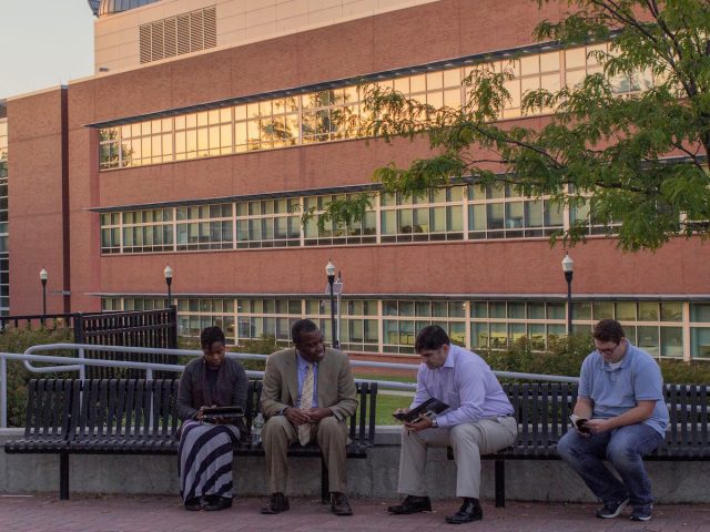 Four people sit on a bench in front of Science Hall at sunset.