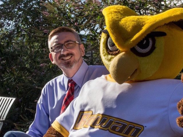 Senior Vice President Jeff Hand sits on a bench with the Rowan mascot giving a thumbs up