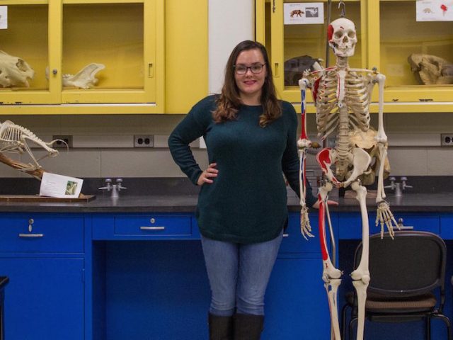 student sits in museum lab next to skeleton