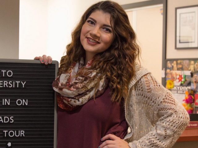 Admissions ambassador stands near sign.