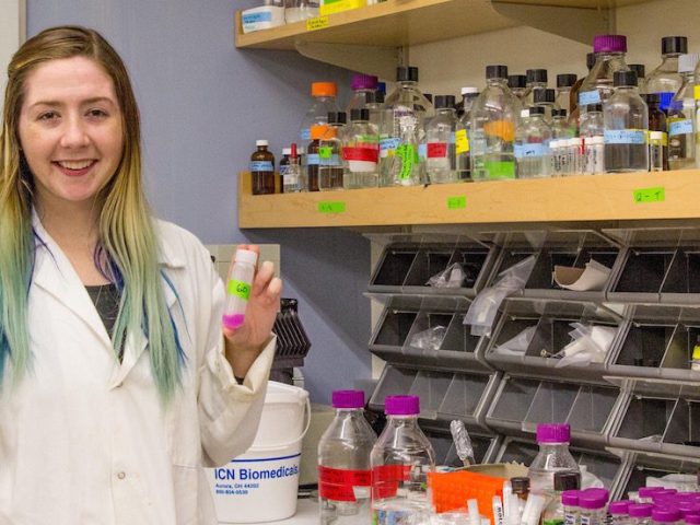 biochemistry major stands near chemistry equipment