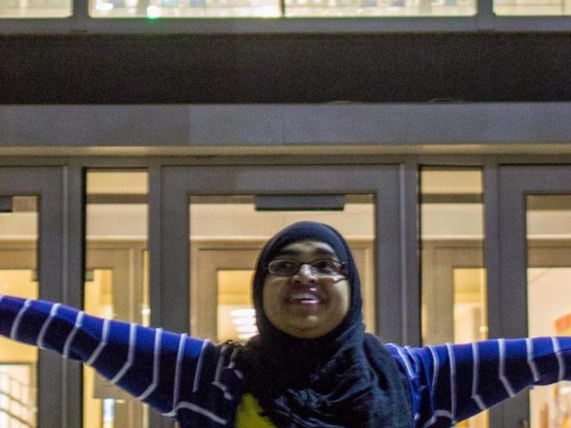 Naveen stands arms outstretched in front of stained glass at James Hall