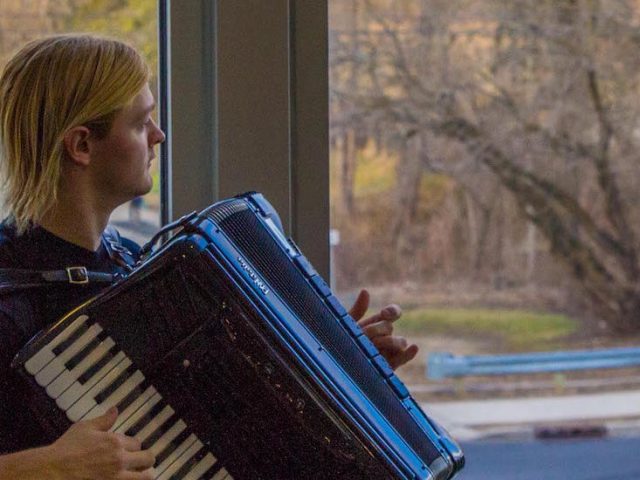 Steve looks out the window at the Glassboro water tower while playing accordian