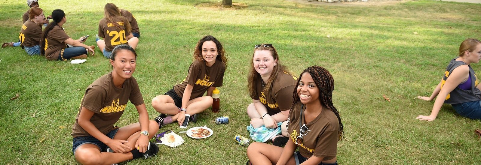 four girls wearing brown Rowan t-shirts sit on the grass