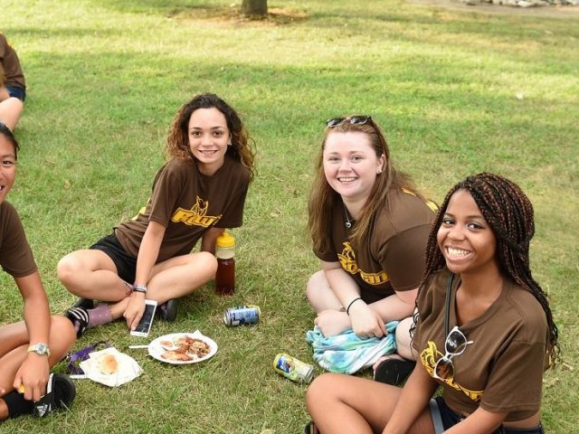 four girls wearing brown Rowan t-shirts sit on the grass