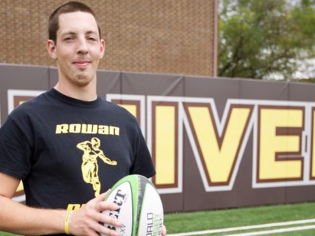 student stands on rowan football field holding a football