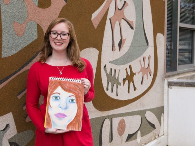 Rowan student Melissa holding her drawing outside Westby art building