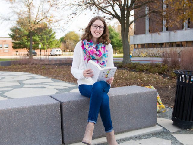 Rowan student Chrissie outside of Robinson Hall reading a book