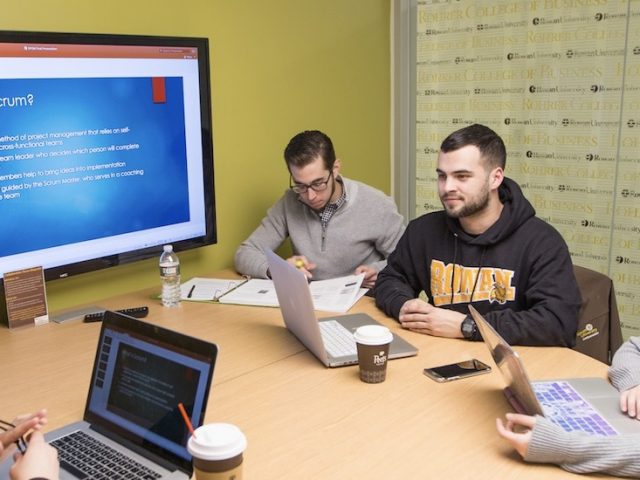 Carlo sits at a collaboration room in Business Hall with other students