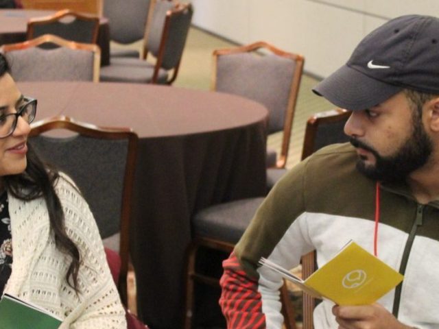 Two students sit at a table speaking to each other about the event.