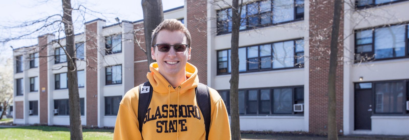 Scott T. is a resident assistant in Mullica Hall, wearing a yellow sweatshirt that says Glassboro State