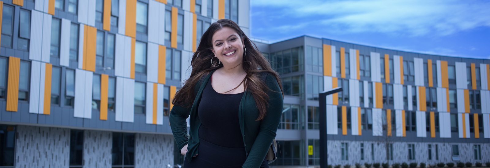 Rowan University student Serena stands with a hand on her hip outside of Holly Pointe Commons.