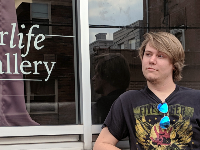 Justin stands next to the glass storefront of Wanderlife Gallery