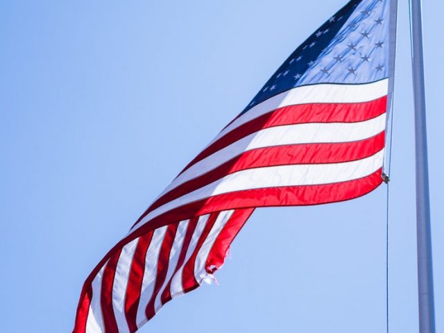 American flag waving in sunshine with blue sky in background