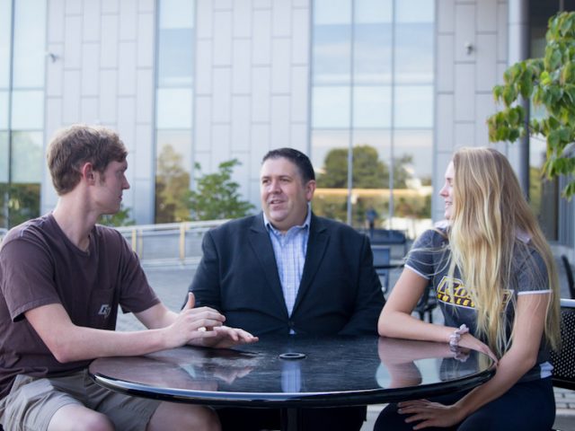 Eric Liguori sitting outside with two students outside the Rohrer College of Business