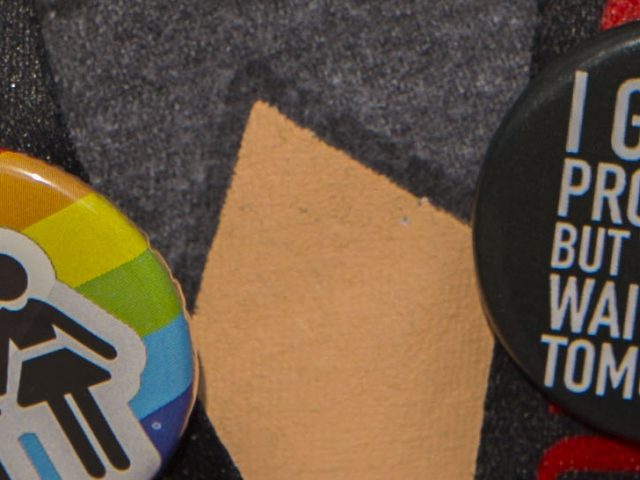 close up of buttons on students lanyard - rainbow button showing black colored stick figures in love and black button that says I got 99 problems but they can wait until tomorrow