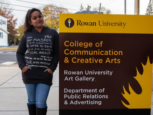 Aysha outside College of Communication and Creative Arts sign