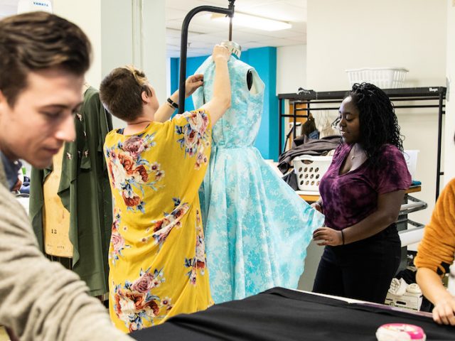 Three students and the costume shop professor work together pinning curtains