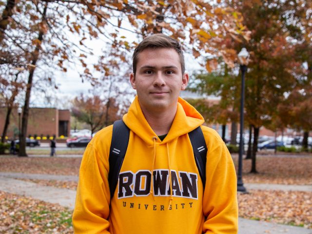 student in Rowan hoodie outside in front of fall leaves and trees