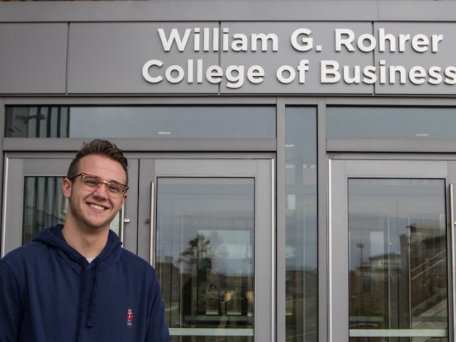 A Rowan student in a blue sweater standing outside the Business Building