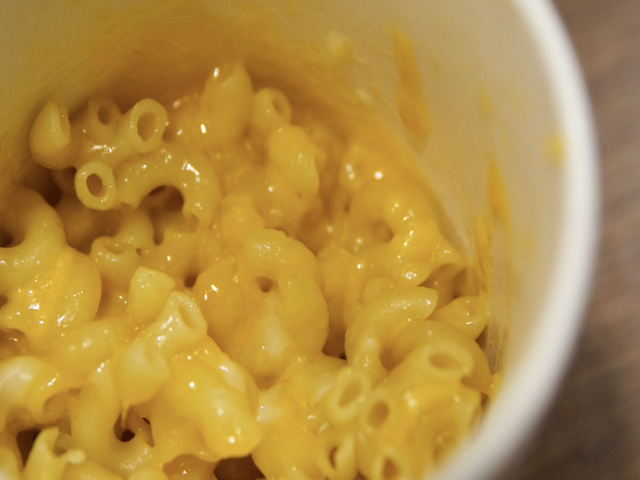 A whilte mug full of macaroni and cheese.