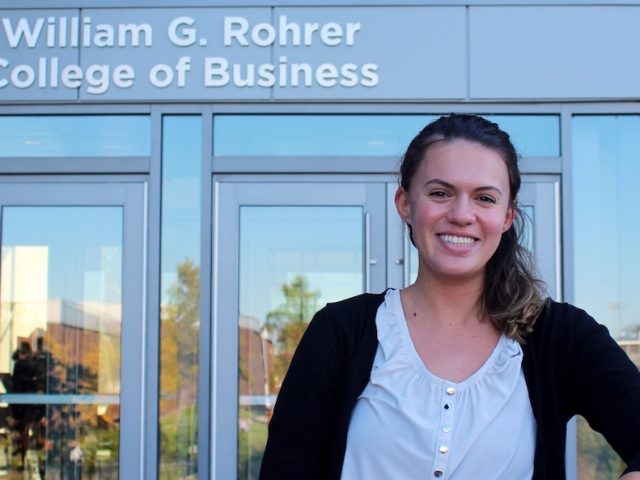 Elizabeth stands in front of the business building, leaning on a post