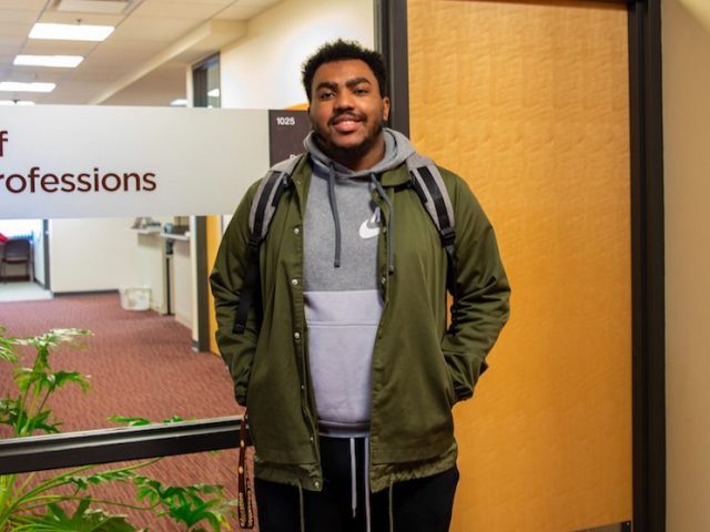 Marcus standing inside James Hall near the Praxis Lab in jacket and bookbag on