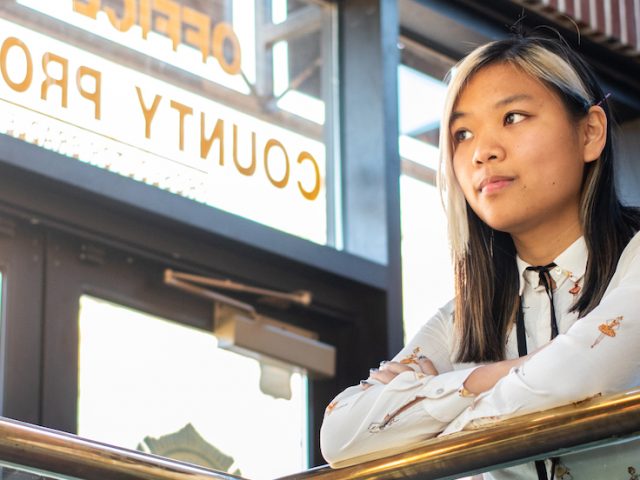 Young lady leaning against hand rail looking off into the distance thinking of all the possibilities the world offers in white button down shirt