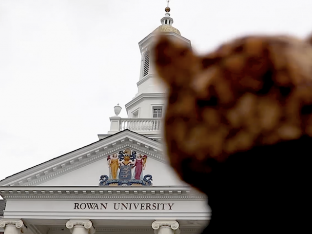 blurred figure in foreground with Rowan University brick and marble building in background