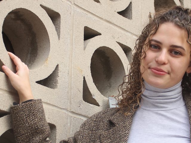 Jenny stands in front a brown concrete wall