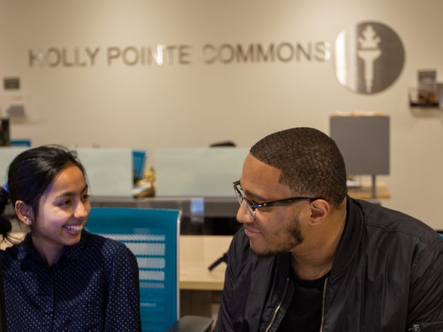 two students inside Holly Pointe behind front desk smiling at each other