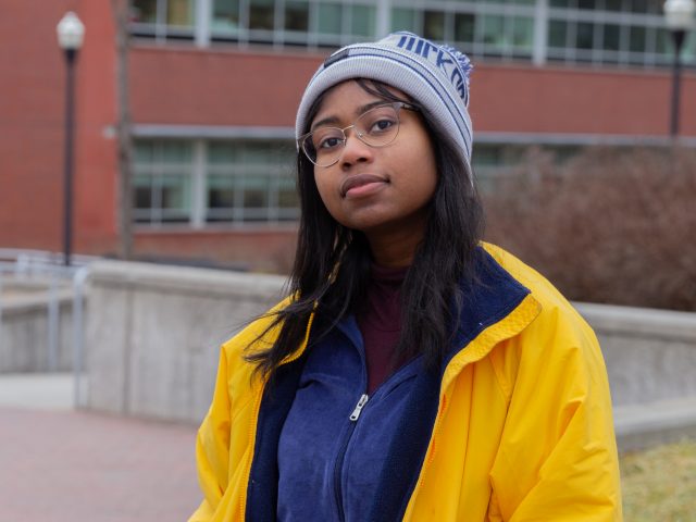 A student wearing a beanie, yellow jacket and blue sweater