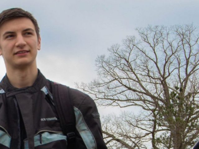 Student stands next to his green motorcycle wearing a black leather riding jacket