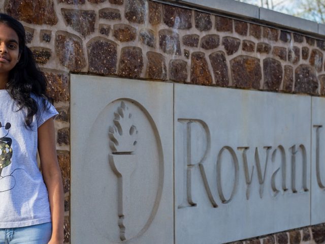 Student outside at Rowan University brick sign out front of Holly Pointe