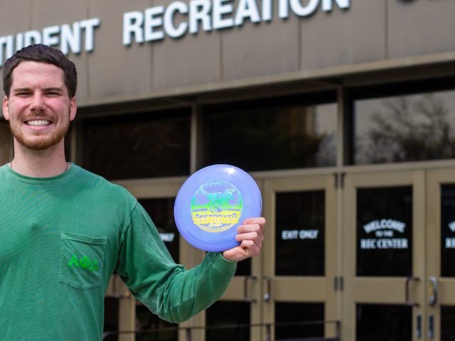 Austin out front of the Rec center holding frisbees up outside