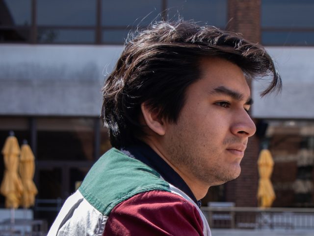 young male student leaning over a railing with a contemplating look on his face