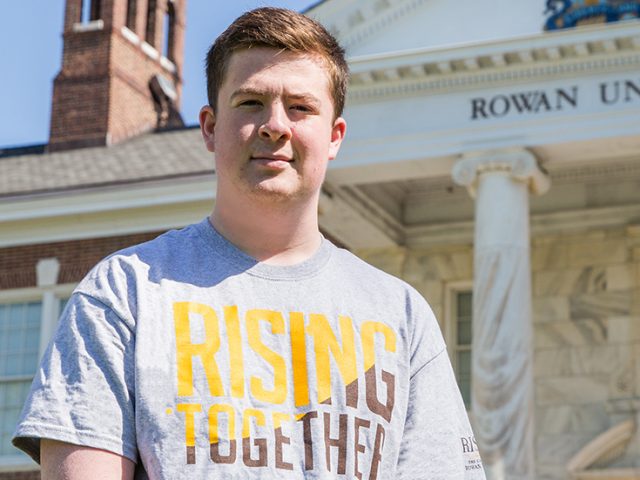 Jason, wearing a Rising Rowan shirt, standing outside Bunce Hall