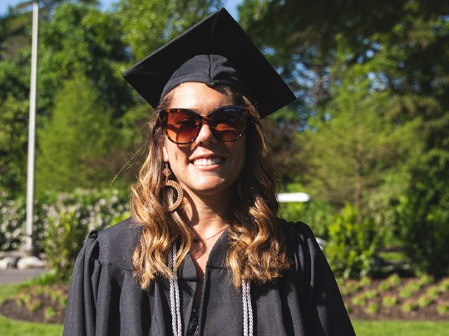 Allyson stands in her cap and gown on the Bunce Green