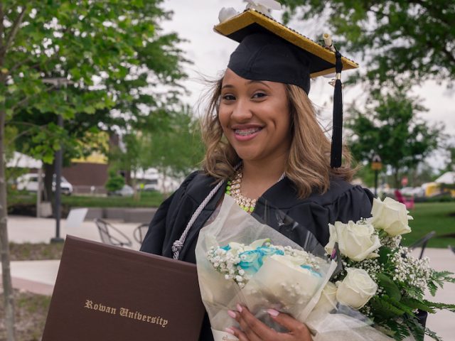 Ciera standing outside in her graduation gown holding a boquet of flowers