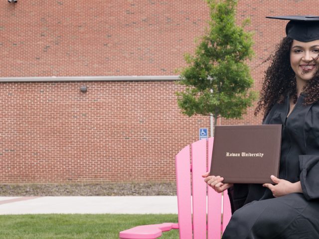 Eduarda in her graduation gown sitting on a pink wooden chair