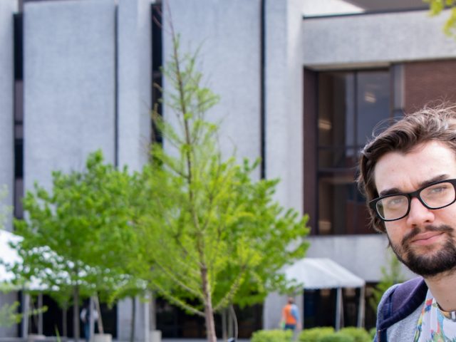 Young male student leaning against bridge with stone building in the background