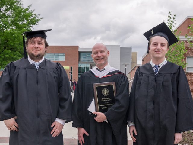 history grads pose with professor, wearing graduation gowns at Rowan University