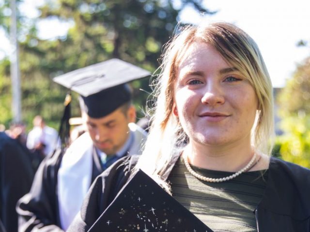 Kelsey, in her graduation gown, holding her decorated cap