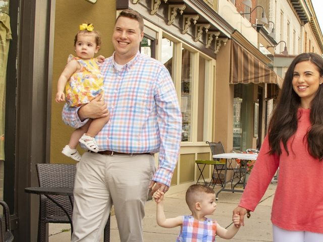 Family of four strolling down a side walk on the main street of a town