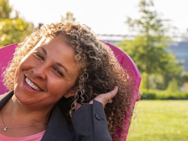 Woman sitting in pink lawn chair laughing while the sun shines down