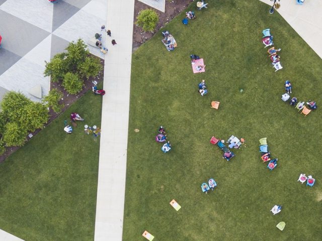 Aerial view of multiple people sitting in lawn chairs in a grassy town square