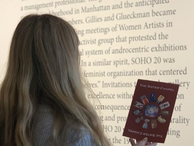 Two girls in the art gallery looking at The Sister Chapel Pamphlet