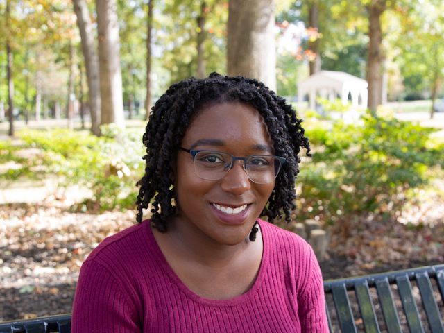 Jessica Hassell, a Higher Education Administration track graduate student and author of story, sits in woods on Rowan University's campus