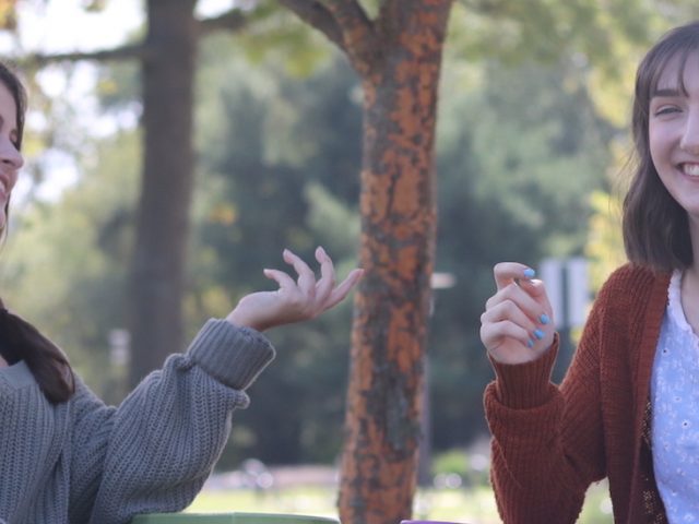 Mattie and her friend chatting outside on a grassy lawn.